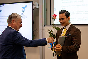 Die beiden Personen stehen sich gegenüber. Im Hintergrund ist noch die Präsentation des Preisträgers zu sehen.