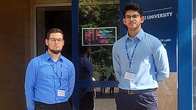 Die Promovenden Jan Bartelt und Yadu Krishnan Krishnakumar stehen vor dem Eingang zur IIPhDW Konferenz an der WSEI University im polnischen Lublin.