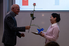 Die beiden Personen stehen sich gegenüber. Im Hintergrund ist noch die Präsentation der Preisträgerin zu sehen.