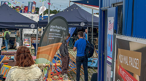 Außenbereich vor dem Stand der Hochschule Wismar mit Banner und mehreren Personen im Gespräch auf einem Außenbereich mit Zelten und Informationsmaterial.