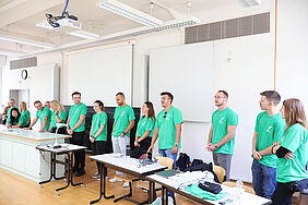 Es sind 15 Studierende zu sehen, die T-Shirts in der Fakultätsfarbe grün anhaben. Die meisten lachen oder lächeln.