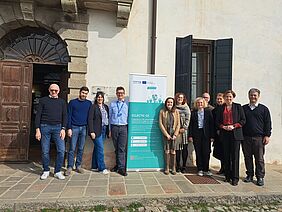 A group of project partners stands in front of a historic building next to a roll-up banner for the Interreg project ECLECTIC-CE and looks into the camera.