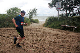Ein Läufer dicht am Warnemünder Strand kämpft trotz grauer Wolken, stürmischen Winds und Strandsand auf der Strecke des 6-Seemeilen-Laufs.