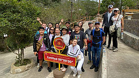 15 Studierenden haben sich hinter einem Schild, das die Äquatorlinie kennzeichnet aufgestellt. Sie freuen sich sichtlich.