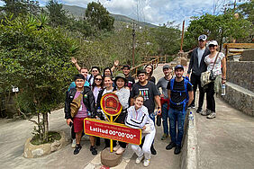 15 Studierenden haben sich hinter einem Schild, das die Äquatorlinie kennzeichnet aufgestellt. Sie freuen sich sichtlich.