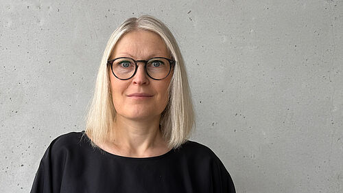 Die Person ist im Porträt vor einer Betonwand zu sehen.