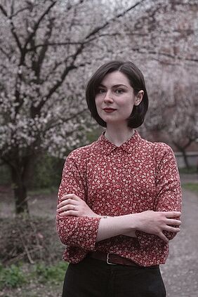 Es ist der Oberkörper der Person zu sehen, im Hintergrund ein Kirschbaum in voller Blüte.
