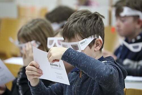 Eine Junge versucht mit einer Brille auf der Nase, dicht über eine Blatt gebeugt, einen Text zu lesen.