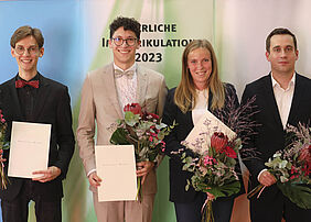 Die vier Ausgezeichneten stehen mit BLumen und Urkunden in der Hand vor einer Bannerwand, auf der Feierliche Immatrikulation 2023 steht.