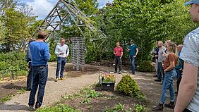Hochschulangehörige stehen in einem Garten im Kreis um Prof. Hillmann herum, der eine Rede hält.