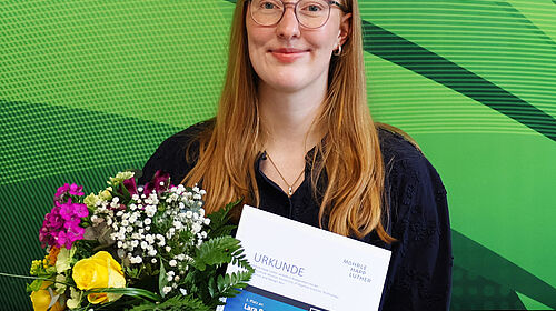 Lara Baumbach hält Urkunde und Blumenstrauß nach der Auszeichnung ihrer Bachelorarbeit.