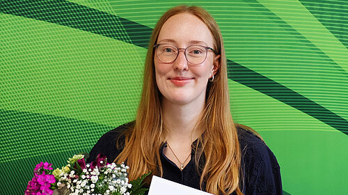 Lara Baumbach hält Urkunde und Blumenstrauß nach der Auszeichnung ihrer Bachelorarbeit.