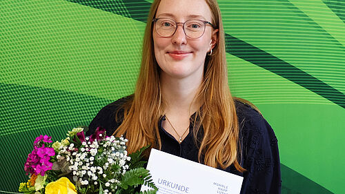 Lara Baumbach holds her certificate and a bouquet of flowers after receiving an award for her bachelor’s thesis.