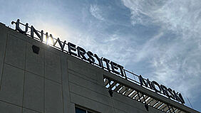 Es ist der Schirftzug der Universität an der Dachkante zu sehen. Die Sonne scheint direkt durch einen Buchstaben.