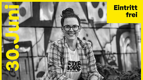 Eine Frau mit dunkler Brille lächelt ins Bild, sie trägt eine karierte Jacke