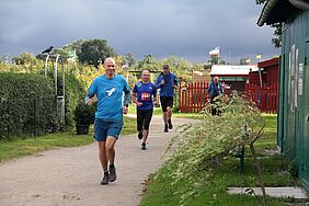 Vier Läufer sind auf den letzten Metern ins Ziel durch die Gartenanlage „Zum Moor“ zu sehen.