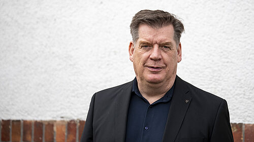 Professor Lau steht vor einer Hauswand im Freien. 