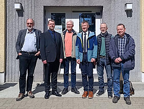 Die sechs Person stehen nebeneinander vor einem Hauseingang.