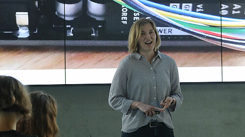 Es ist die Studentin Carolin Grodt während des Science Slam 2022 zu sehen, wie sie auf ein Bild ihrer Präsentation zeigt, dem Publikum zugewandt.