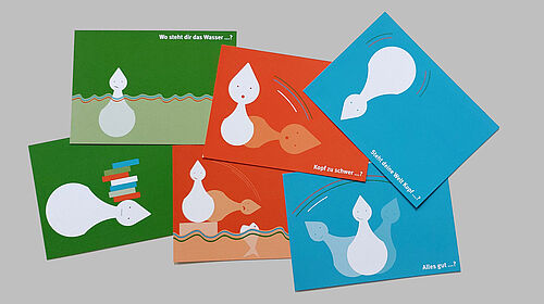 Es sind sechs Postkarten zu sehen, wobei jeweils zwei als Hintergrundfarbe die Fakultätsfarben türkis, grün und orange zeigen.