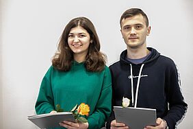 Es sind Sofia und  Mykhailo mit Urkunde und einer Blumen in der Hand zu sehen.