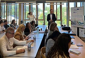 Project Partners at the All Partner Meeting in Odsherred. Meeting participants seated at tables in a bright seminar room with large windows, while a speaker addresses the group at the front.