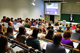 Im Hörsaal ist von hinten, über die Köpfe der Teilnehmenden hinweg, Prof. Hölterhoff zu sehen.