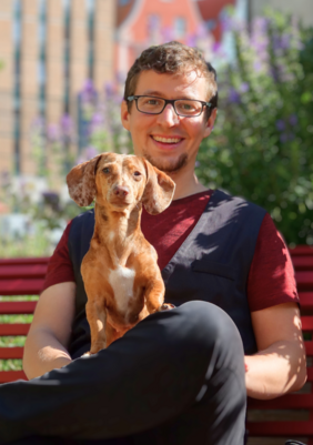 Die PErson sitzt auf einer Bank und hat einen rotbraunen Hund auf ihrem Schoß.