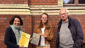 Research on environmental liability law presented Three people are standing in front of a brick façade; two of them are holding specialist legal publications.