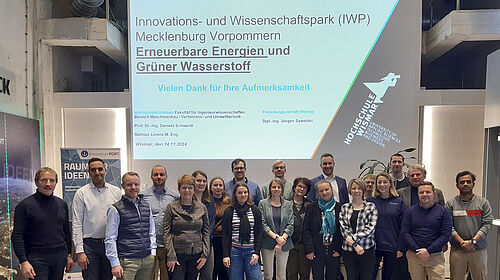 Die 21 Personen stehen in zwei REihen nebeneinander. Im Hintergrund ist das Präsentationsbild an der Wand zu erkennen.