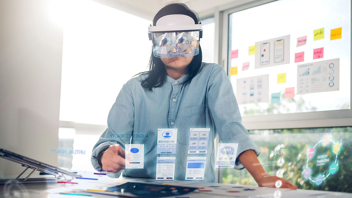 Introduction_Image_Symbolbild_WI_Master_SL_2023 Introduction_Image Studiengang Wirtschaftsinformatik Master Eine Frau mit AR Brille sieht vor sich virtuelle Tabs vor einem Tisch