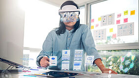 Introduction_Image Studiengang Wirtschaftsinformatik Master Eine Frau mit AR Brille sieht vor sich virtuelle Tabs vor einem Tisch