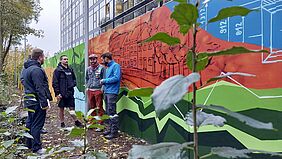 Es sind fünf Personen vor der Mauer mit dem Graffiti zu sehen.