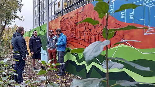 Es sind fünf Personen vor der Mauer mit dem Graffiti zu sehen.