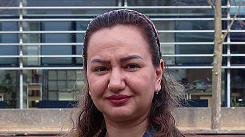 Porträt einer Frau im Freien auf dem Wismarer Campus vor einem modernen Hochschulgebäude. Sie trägt eine Jeansjacke und blickt in die Kamera.