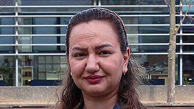 Porträt einer Frau im Freien auf dem Wismarer Campus vor einem modernen Hochschulgebäude. Sie trägt eine Jeansjacke und blickt in die Kamera.