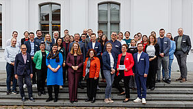 Alle 40 Personen stehen auf vier Stufen einer Treppe verteilt vor einem Gebäude.