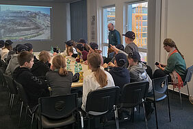 Viele Schüler_innen sitzen an einem Tisch im Beratungsraum eines Bauunternehmens.