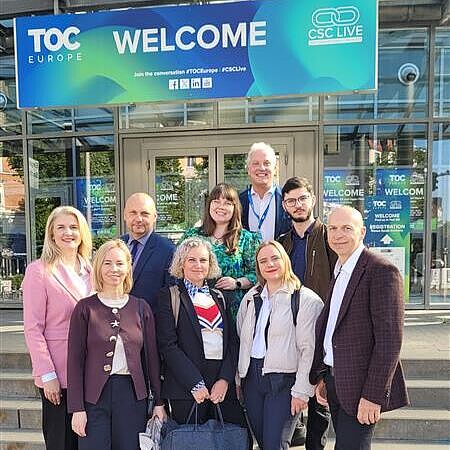 Several project partners from the DigiTechPort2030 consortium are standing outside the entrance to TOC Europe 2026 in Hamburg. Above them hangs a large welcome sign for the trade fair.