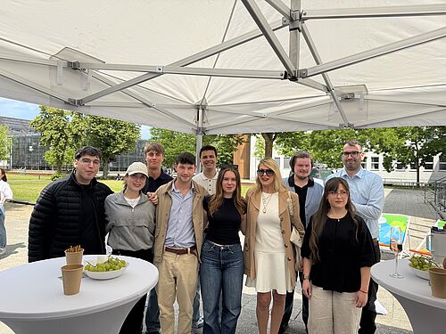 A group of students is standing with Prof. Dr Jantina Nord under a pavilion in front of the university lawn.