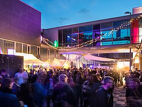 Viele Menschen feiern draußen zwischen den Häusern 7a und 7b während der DIA. Abendstimmung mit tollen Lichteffekten.