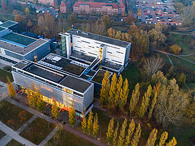 Der dreiteilige Gebäudekomplex ist von oben zu sehen dank einer Drohnenaufnahme. Das Gebäude ist von Bäumen mit Herbstlaub umgeben.