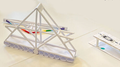 Es ist eine Papierbrücke aus weißem Papier zu sehen. Am rechten Rand befindetsich das Ende eier Paierbrücke auf die ein Auto gemalt wurde.