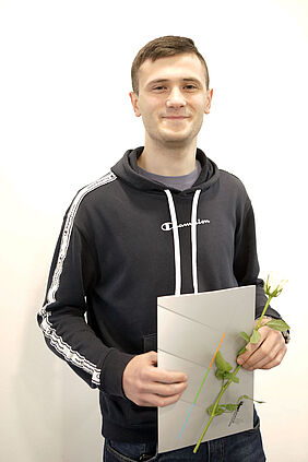 Es ist  der ukrainische Student mit seiner Urkunde und einer Blumen in der Hand zu sehen.