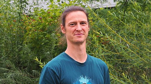 Es ist Prof. Frank Krüger im Porträt vor einer Grünanlage auf dem Campus zu sehen.