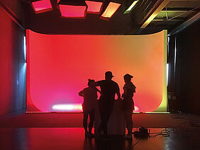 Es ist die Hohlkehle der Fotowerkstatt während eines Lichtworkshops zu sehen - 3 Personen vor einer beeindruckenden rot-Orange-Ausleuchtung