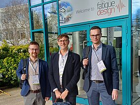 Prof. Dr.-Ing. Ralf Glienke steht mit zwei Kollegen vom Fraunhofer IGP vor dem Eingang zur 11. Internationalen Fatigue-Design-Konferenz in Frankreich