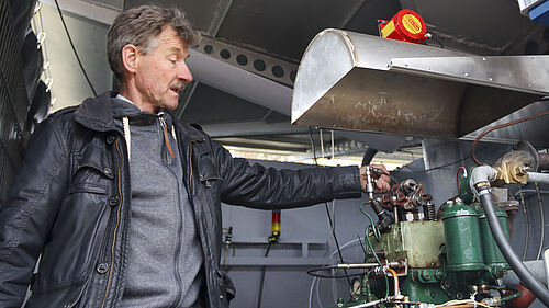 Die Person hält ein Ventil in der Hand, welches er über den historisch anmutenden Motor hält.