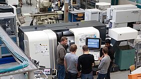 Fünf Personen stehen vor einer rund 2 Meter hohen und 4 Meter breiten Drehmaschinen. Einer davon ist der Professor, der direkt an der geöffneten Schutztür steht.