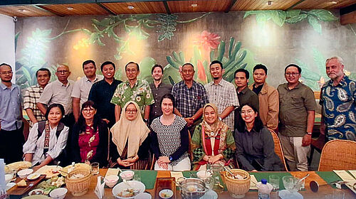 19 Personen stehen bzw. sitzen hinter einem langen Tisch. Auf diesem befinden sich zahlreiche leere Schüsseln, Teller und Gläser.